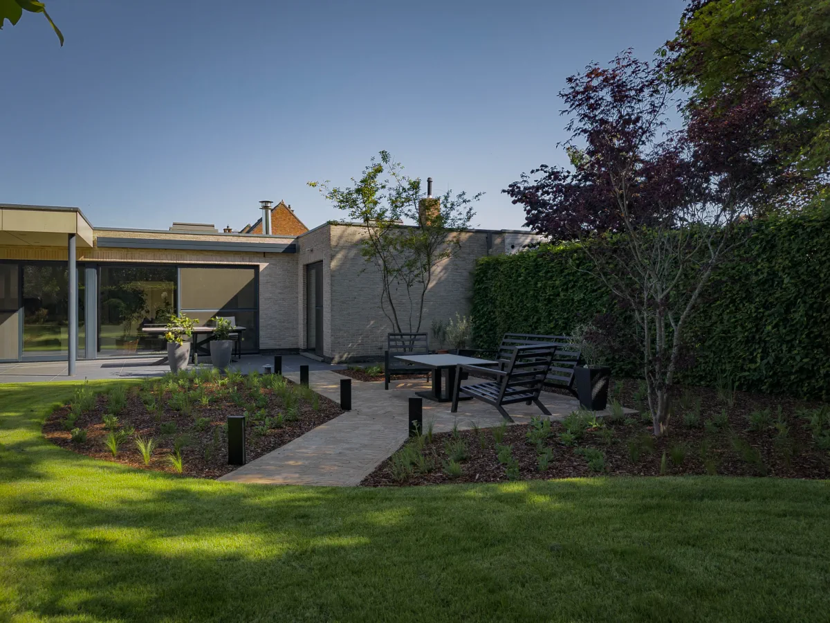 Moderne tuin met een groot functioneel terras tegen de woning en een loungeterras temidden van prairiebeplanting met siergrassen, gerealiseerd in Sint-Niklaas